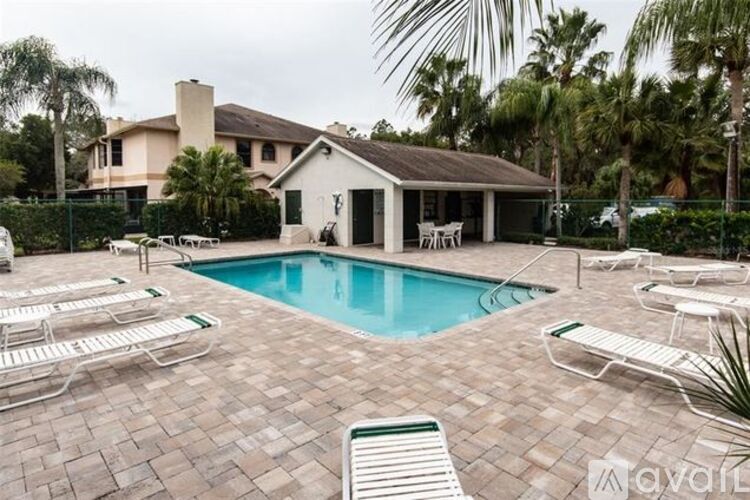 A pool surrounded by lounge chairs and a house in the background.