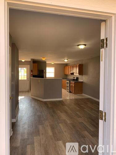 A room with wooden flooring and a kitchen area in the background.