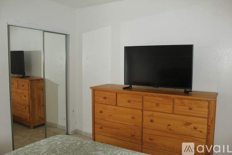 A bedroom with a bed, a dresser with a TV on top, and a mirror.