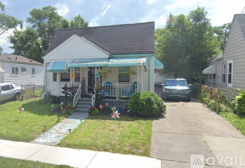 A small house with a blue awning is surrounded by a grassy lawn and a sidewalk.