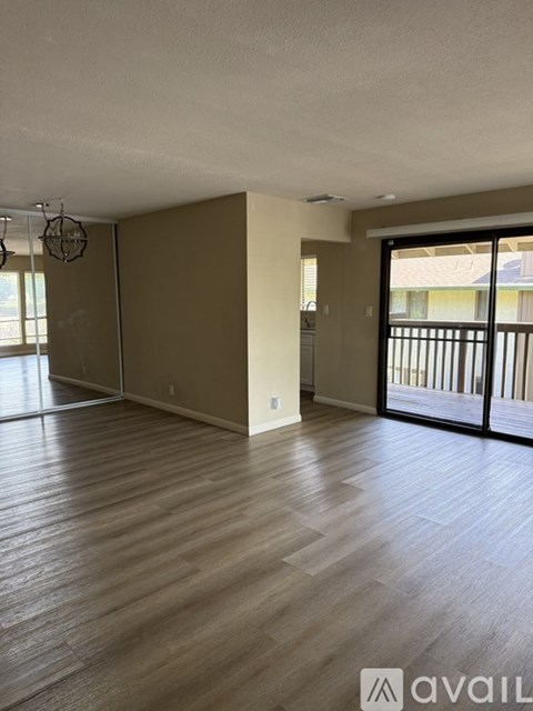 A spacious room with wooden flooring and a sliding glass door leading to a balcony.