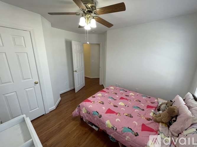 A bedroom with a pink bedspread and a teddy bear on the bed.