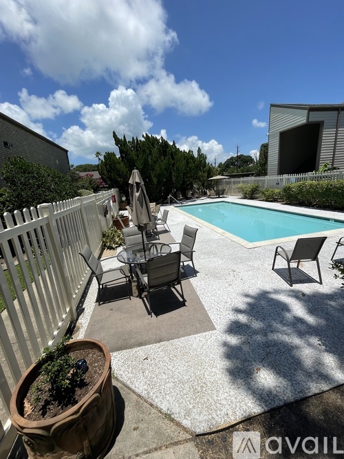 A pool with chairs and a table is surrounded by a white fence.