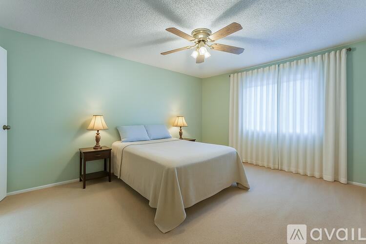 A bedroom with a bed, two lamps, and a ceiling fan.