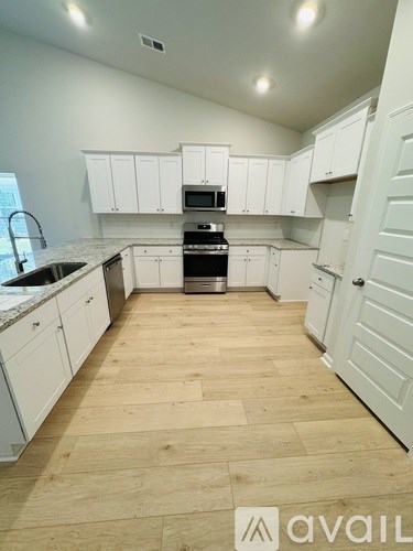 A kitchen with white cabinets and wooden flooring.