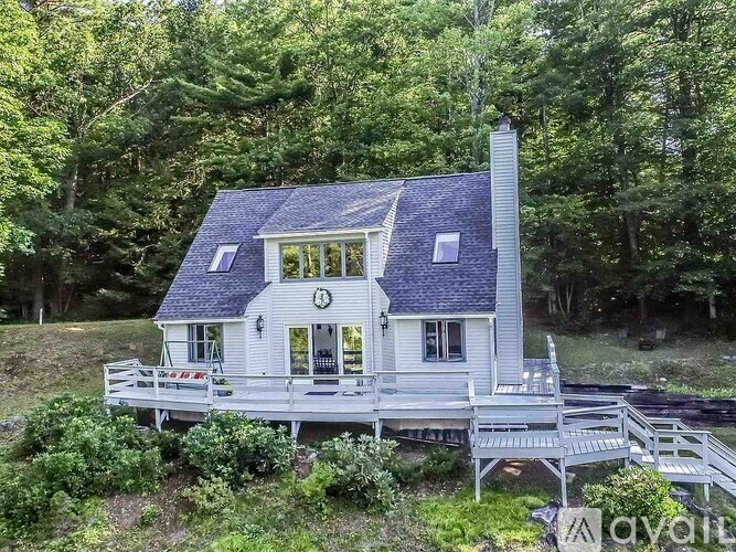 A house with a porch and a chimney is surrounded by greenery.