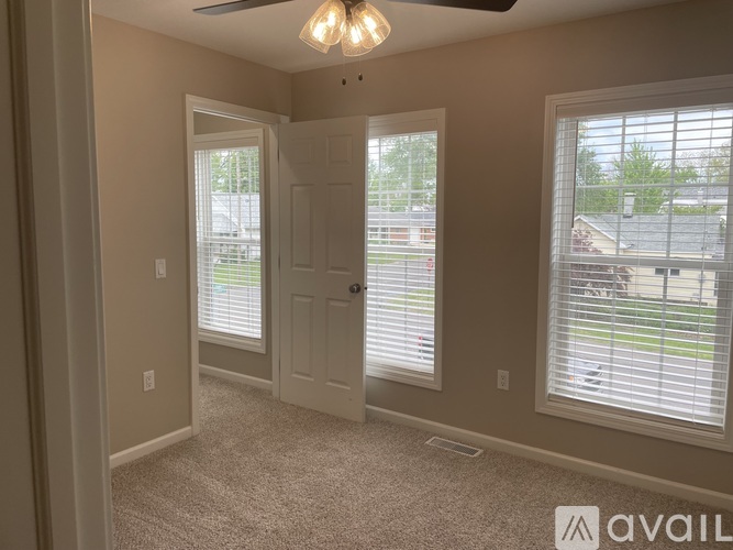 A room with a carpeted floor, a ceiling fan, and a door leading to a balcony.