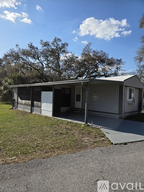 A house with a grey roof and a white fence is surrounded by grass and trees.