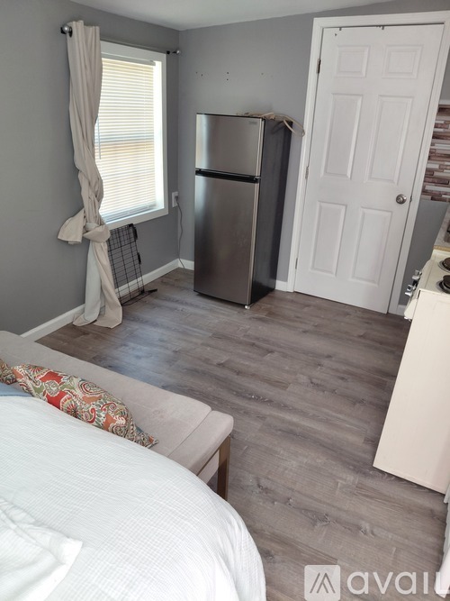 A kitchen area with a refrigerator and a bed with a white comforter.