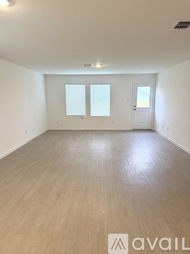 A spacious room with wooden flooring and a door on the right side.