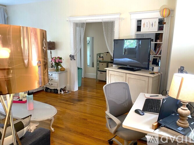 A living room with a television, a desk with a laptop, and a chair.