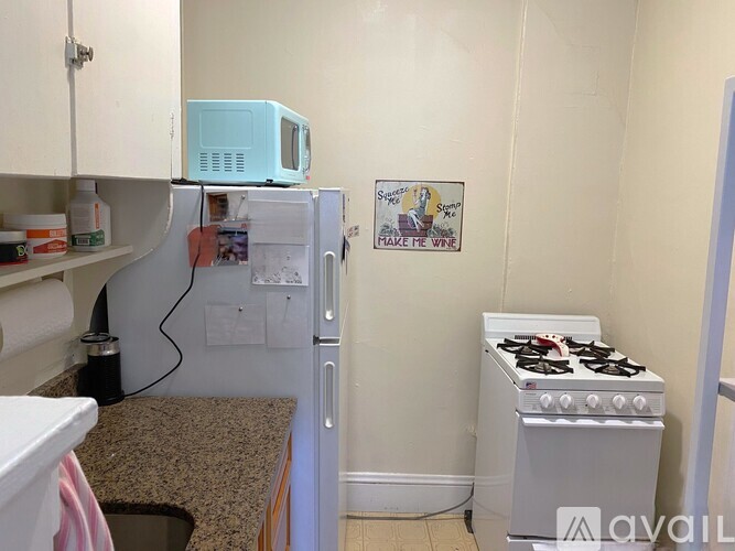 A small kitchen with a blue microwave on top of the fridge and a stove on the floor.