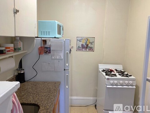 A small kitchen with a blue microwave on top of the fridge and a stove on the floor.