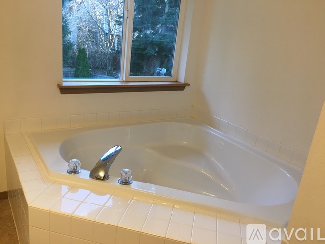 A white bathtub with silver faucets in a bathroom with a window.