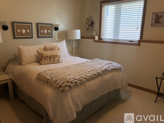 A bedroom with a bed covered in a white blanket and pillows that say "happy".