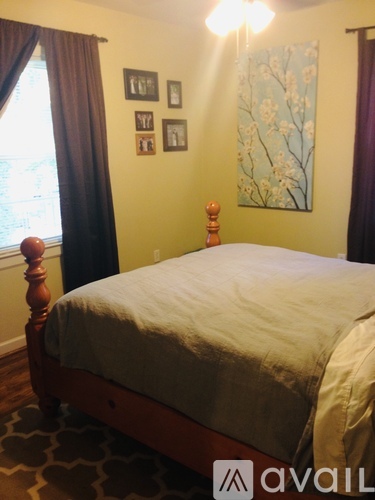 A bedroom with a bed, pictures on the wall, and a window with curtains.