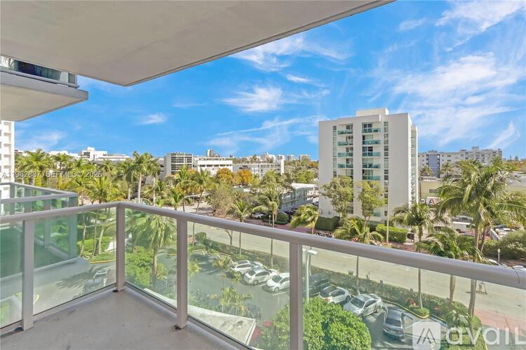 A balcony with a glass railing overlooking a parking lot and buildings.