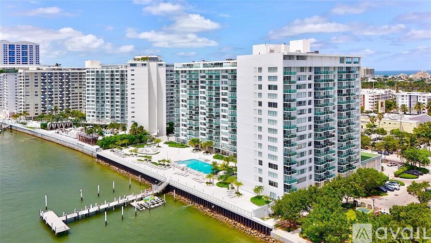 A large white building with a pool is situated next to a body of water.