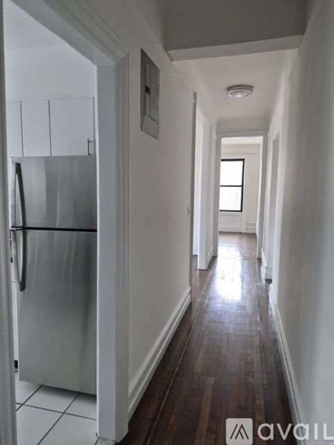 A long hallway with a refrigerator on the left and a light at the end.