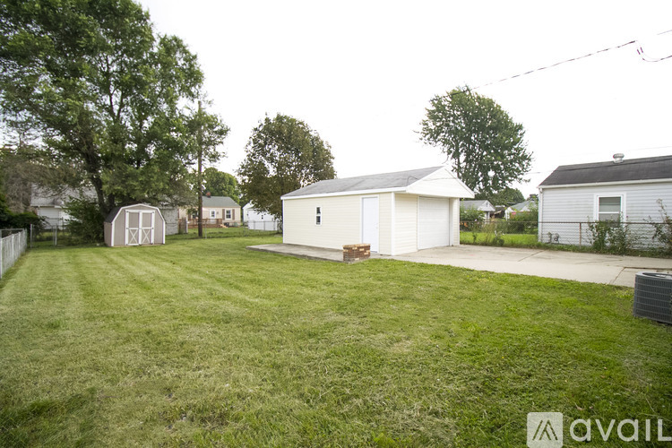 A grassy yard with a white house and a tree in the background.