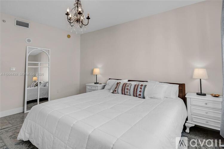A bedroom with a large bed, a chandelier, and a nightstand with a lamp.