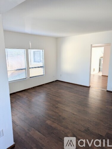 A room with wooden floors and white walls, with a window on the left and a door on the right.