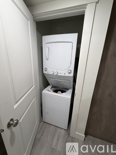 A small white washing machine sits in a narrow space between a door and a wall.