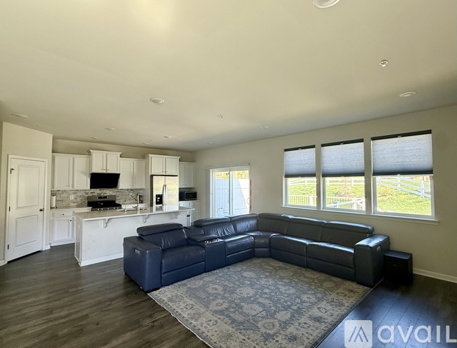 A spacious living room with a black leather sofa and a kitchen area with white cabinets.
