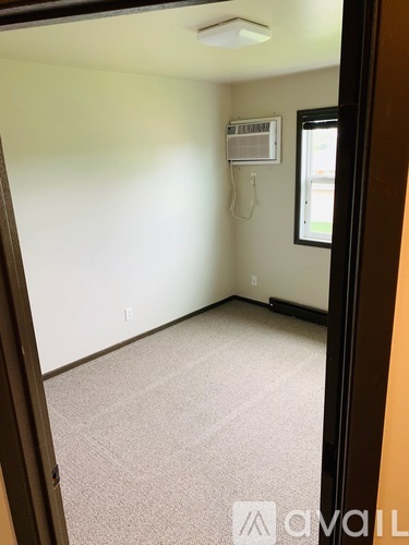 A carpeted room with a window and an air conditioner unit on the wall.