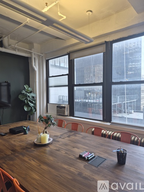 A conference room with a long table and chairs, a vase with a plant, and a view of the city through the windows.