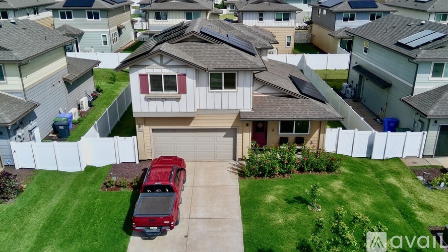A red car is parked in the driveway of a house with a white fence.