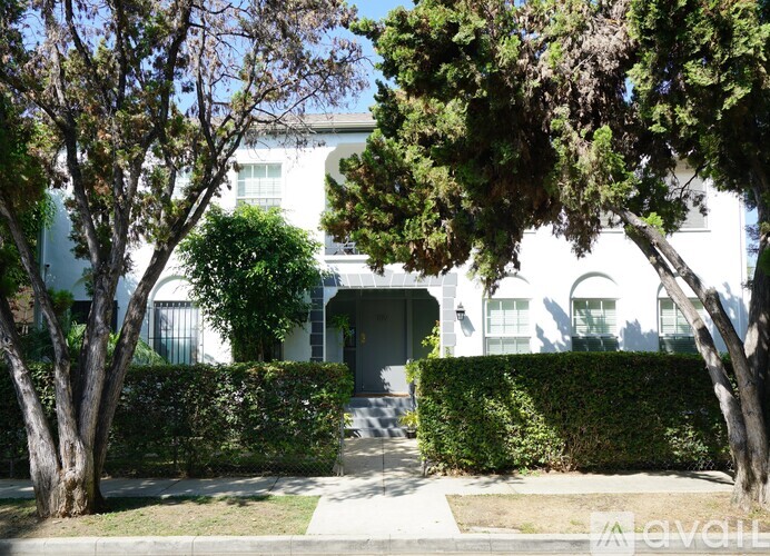 A white house with a grey door is surrounded by green trees.