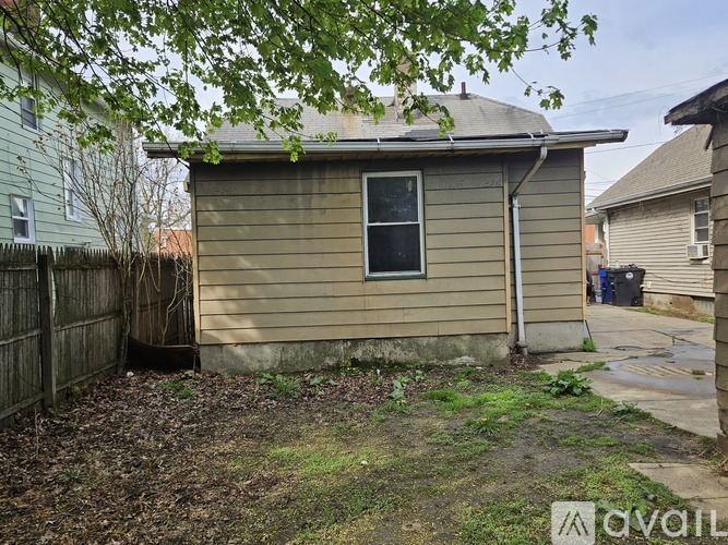 A small house with a window and a door is surrounded by a fence and has a tree in the foreground.