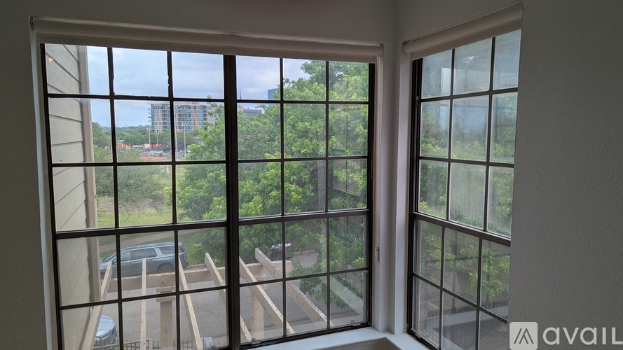 A window with a view of a parking lot and trees.