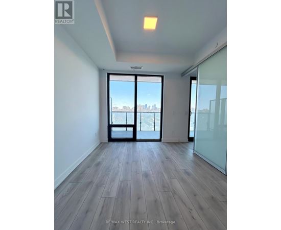 A spacious room with wooden flooring and a view of the city through a large window.