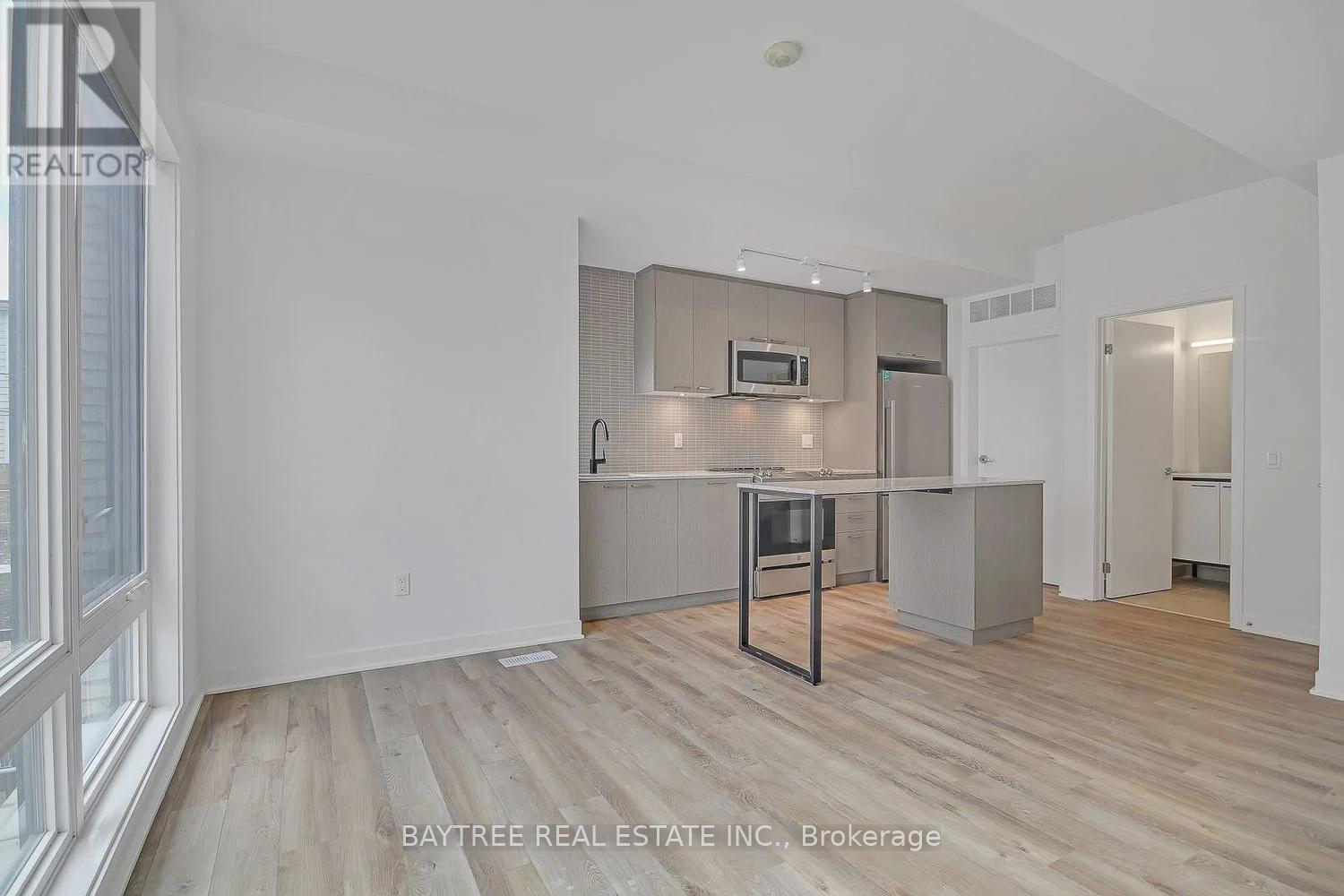 A real estate listing image of a kitchen with white walls and wood flooring.