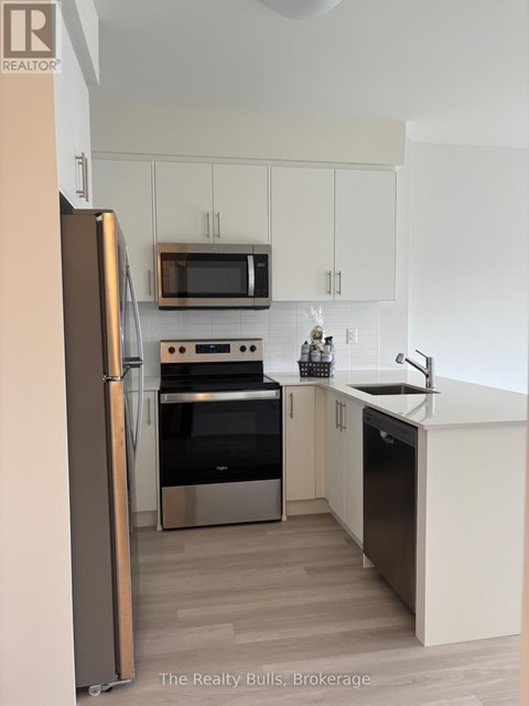 A kitchen with a refrigerator, microwave, oven, and sink.