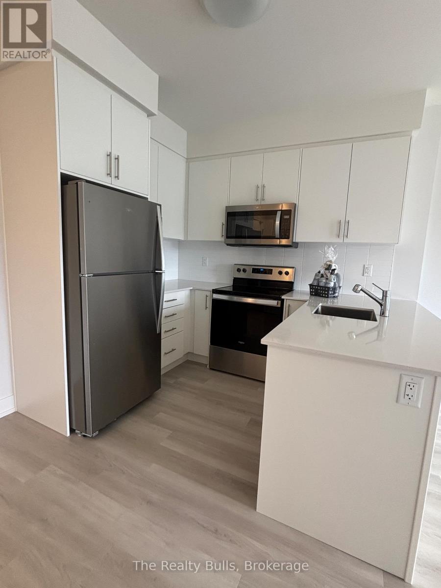 A kitchen with a refrigerator, microwave, oven, and sink.