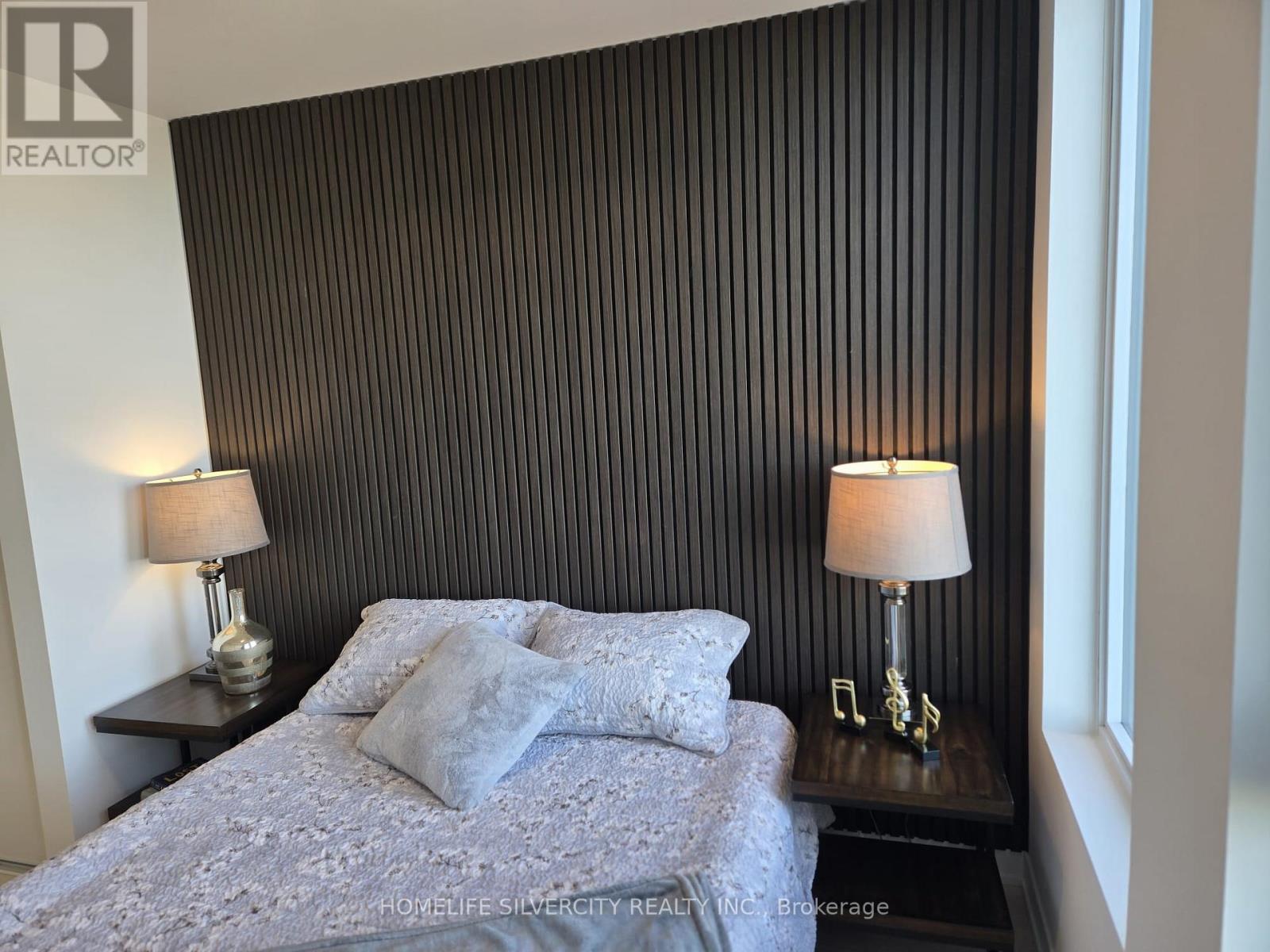 A bedroom with a bed, two lamps, and a striped wallpaper.