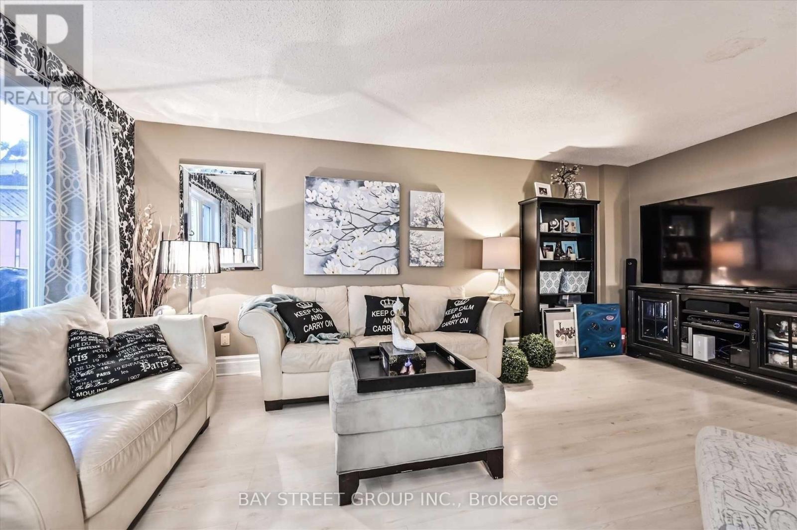 A living room with a white couch, a grey ottoman, and a black and white pillow.