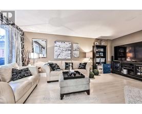 A living room with a white couch, a grey ottoman, and a black and white pillow.