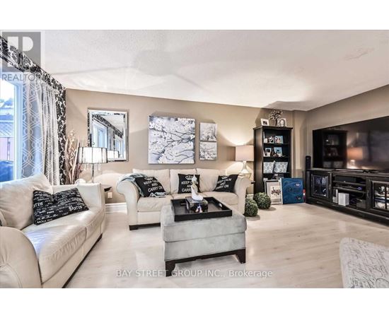 A living room with a white couch, a grey ottoman, and a black and white pillow.