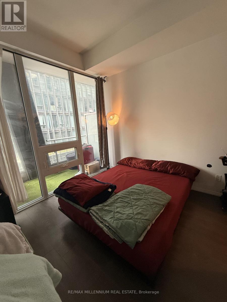 A bedroom with a red bed and a window with a view of a building outside.