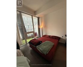 A bedroom with a red bed and a window with a view of a building outside.