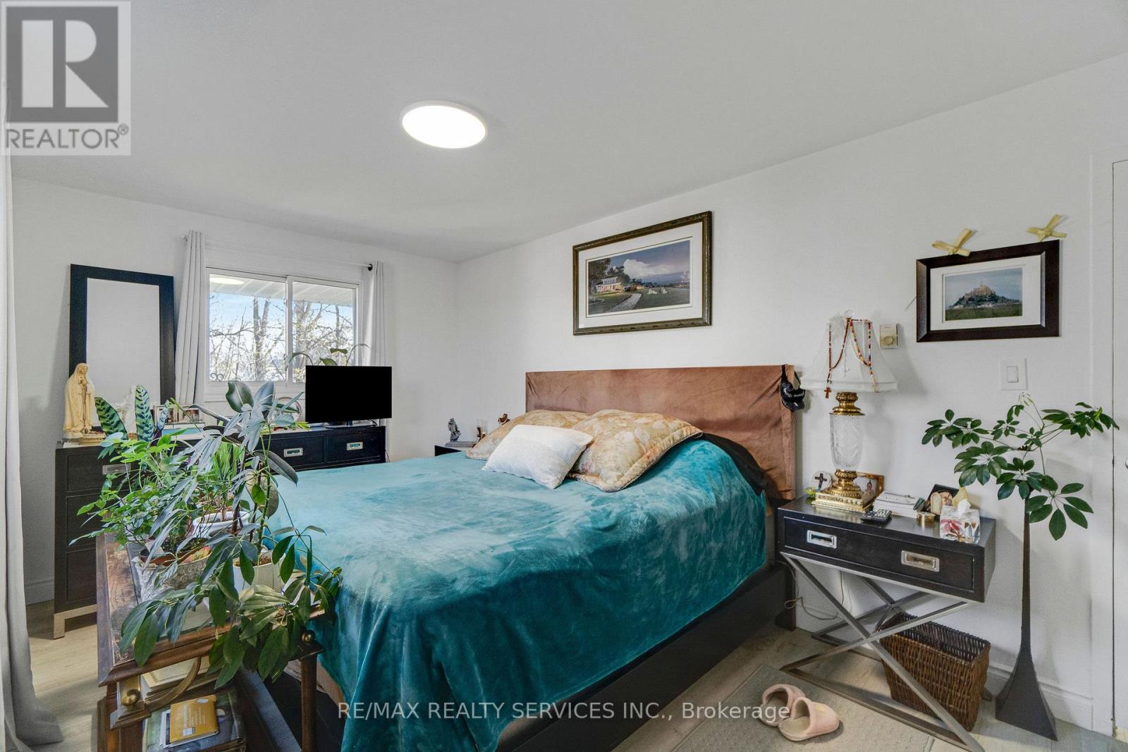 A bedroom with a bed, nightstand, and a plant.