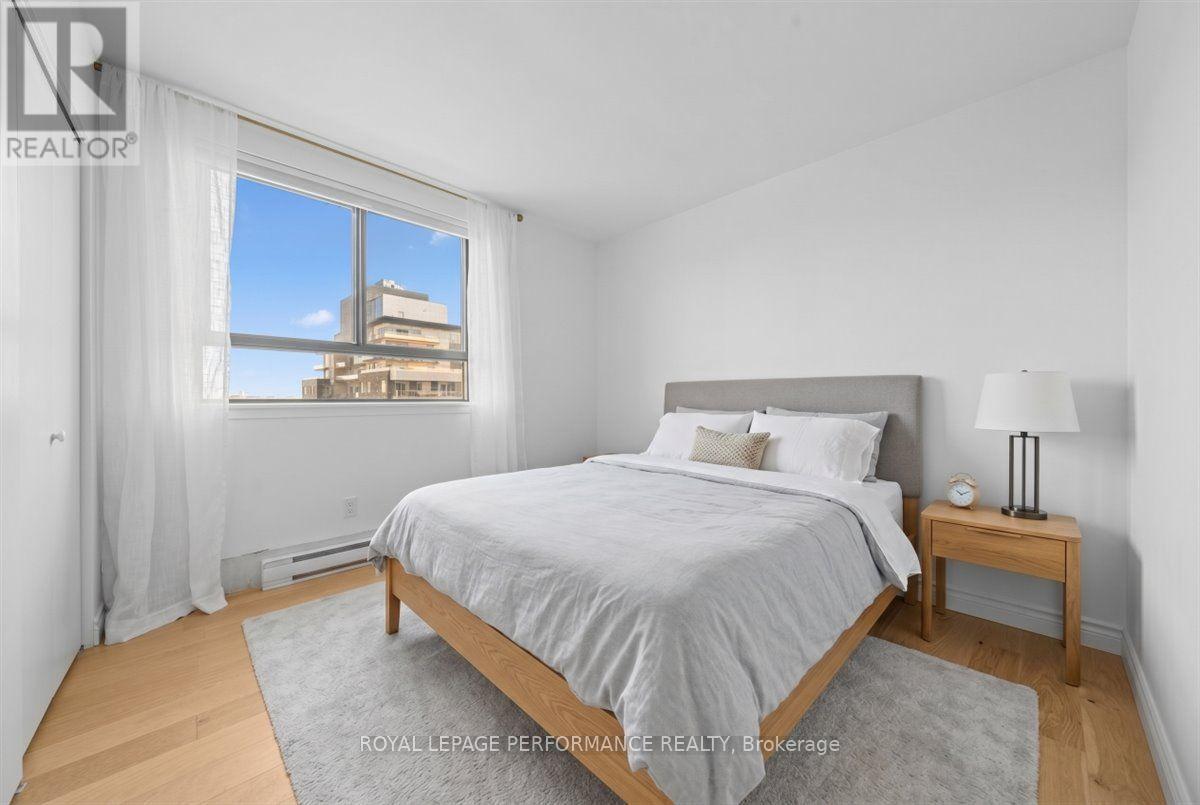 A bedroom with a large bed, a nightstand with a lamp, and a window with a view of a building outside.