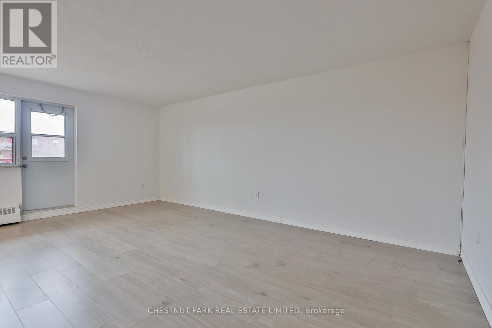A room with a wooden floor and white walls, with a door on the left side.