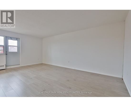 A room with a wooden floor and white walls, with a door on the left side.