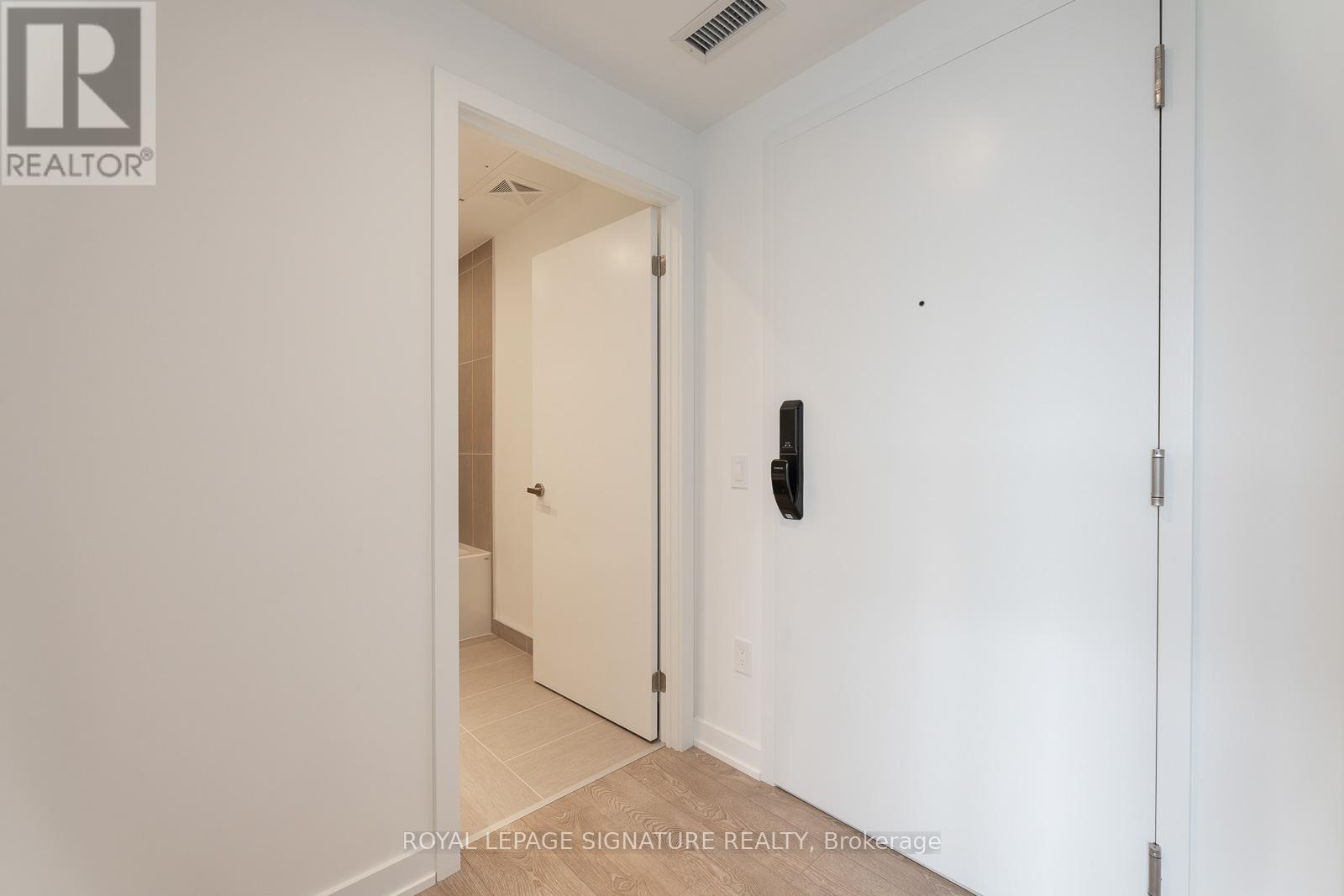 A white hallway with a door on the left and a wall-mounted light switch on the right.