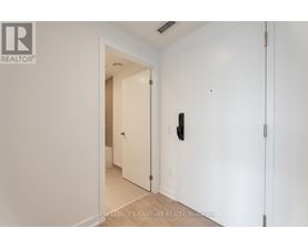 A white hallway with a door on the left and a wall-mounted light switch on the right.